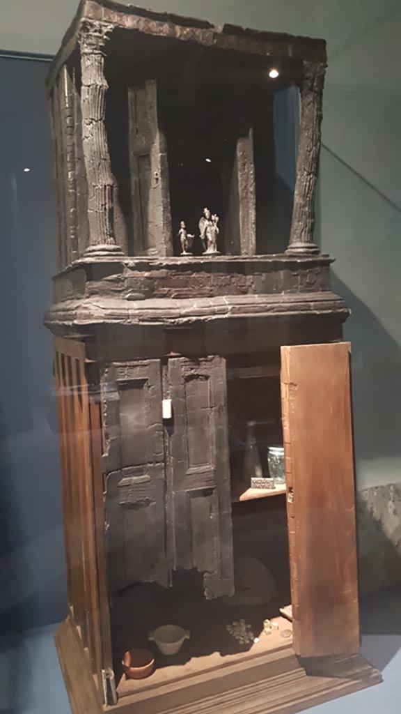 V.31 Herculaneum, August 2023. 
Wooden cupboard, with its upper part in the form of a tiny temple.
This was found in Room 2 in 1934, the room on the right of the entrance corridor.
On display in exhibition entitled – “Materia. Il legno che non bruciò ad Ercolano”.  
Photo courtesy of Maribel Velasco.